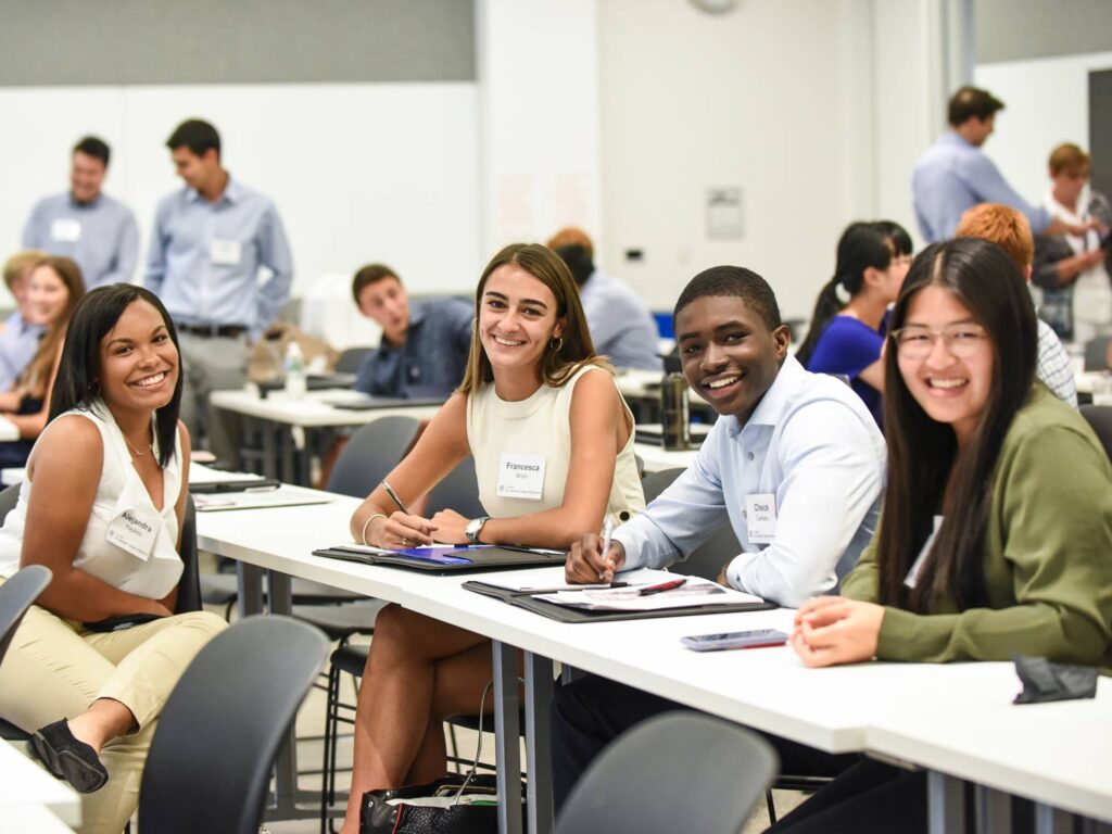 Students sit in a tiered lecture hall listening to a professor.
