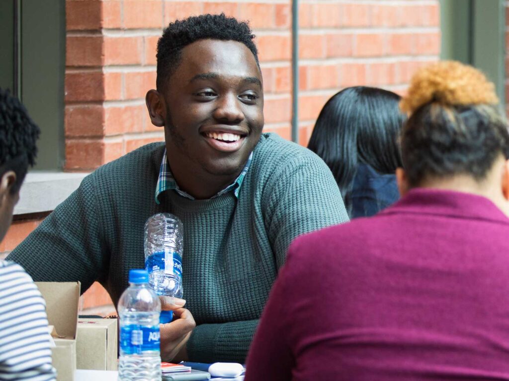 A student sits outside and shares a meal with classmates.