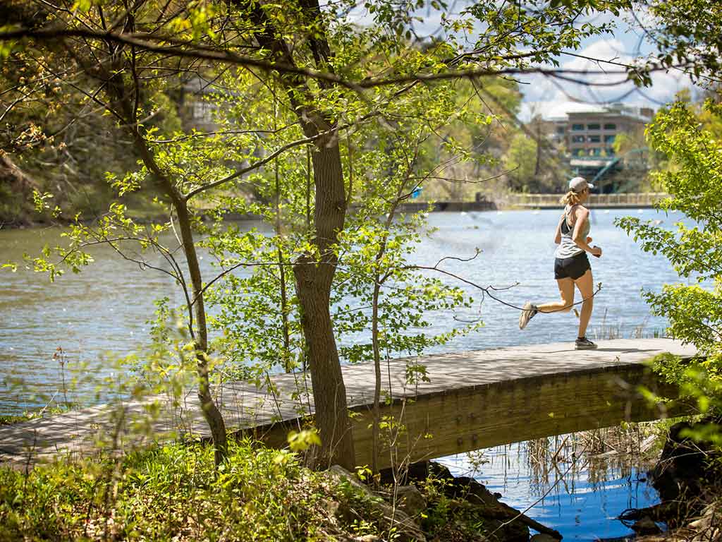 A woman in a baseball hat runs across a small bridge.