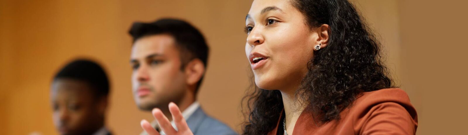 A woman in business attire speaking with two other people out of focus in the background.