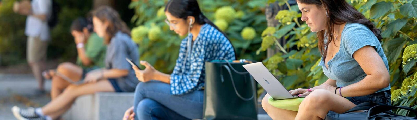 Students sit atop a concrete wall working.