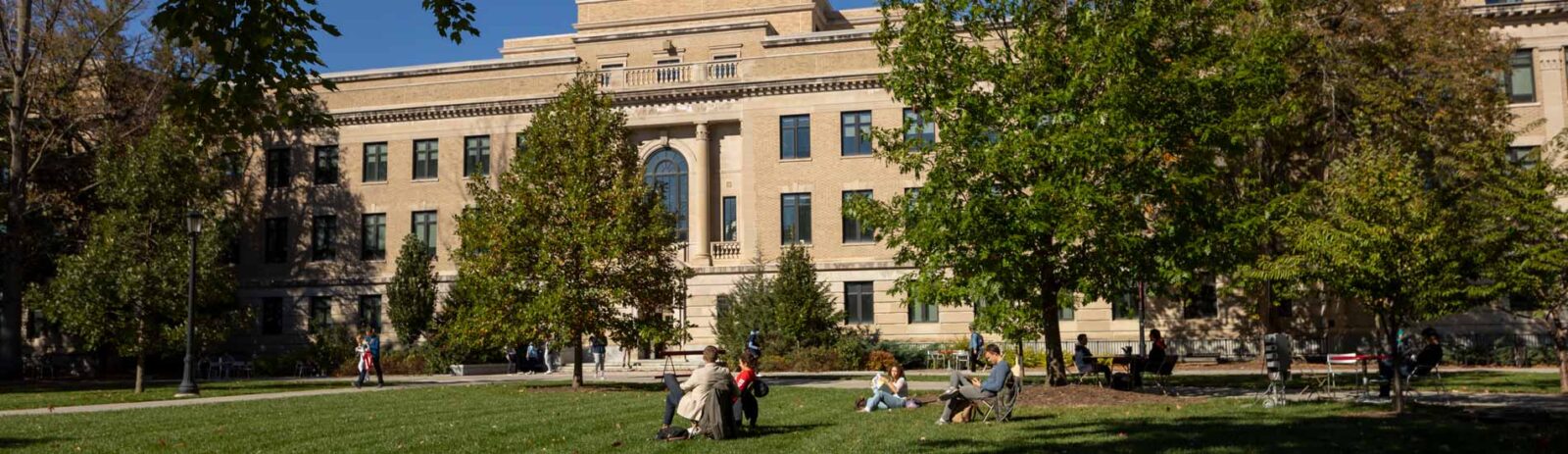 People sit on the ground and in folding chairs on the AG Quad in front of Warren Hall.