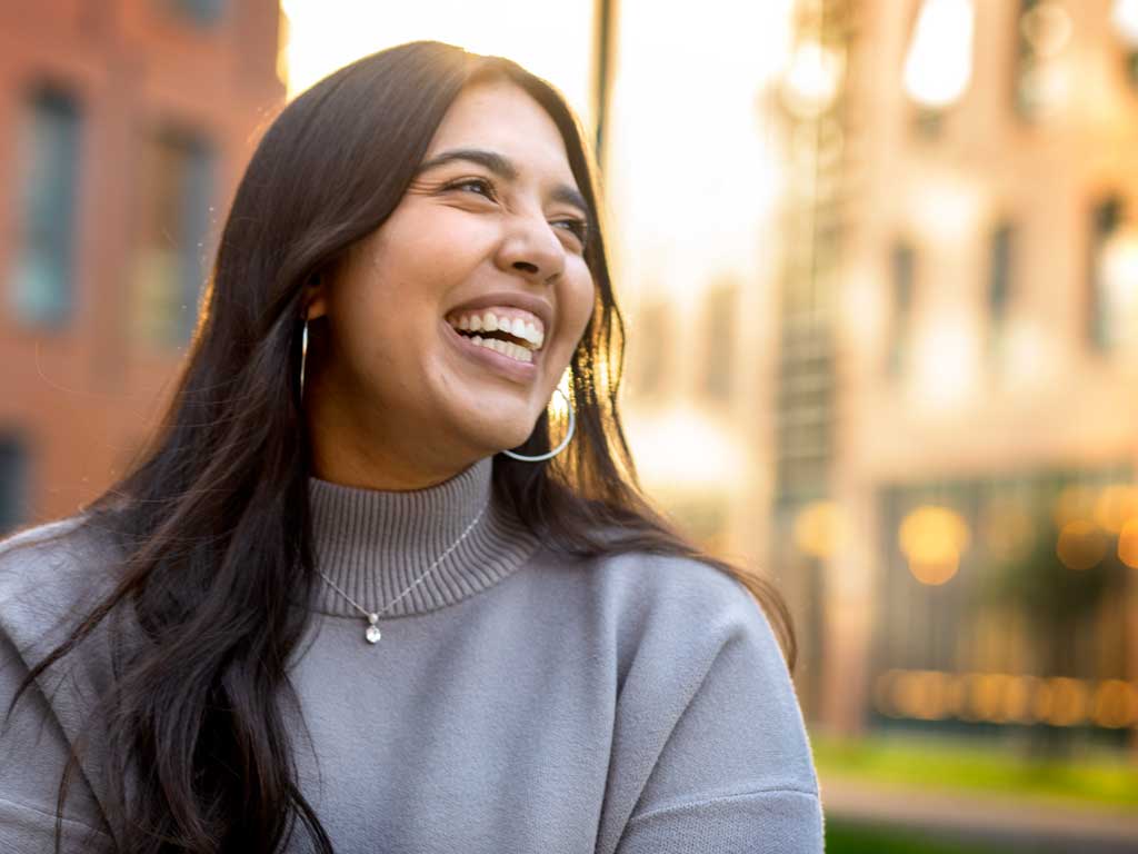 Woman outside smiling and laughing to someone out of frame.