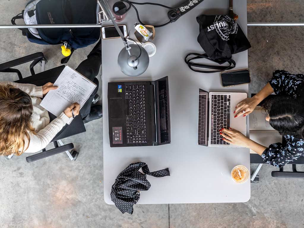 View from above of two woman sitting across from each other at a table and working on laptops.
