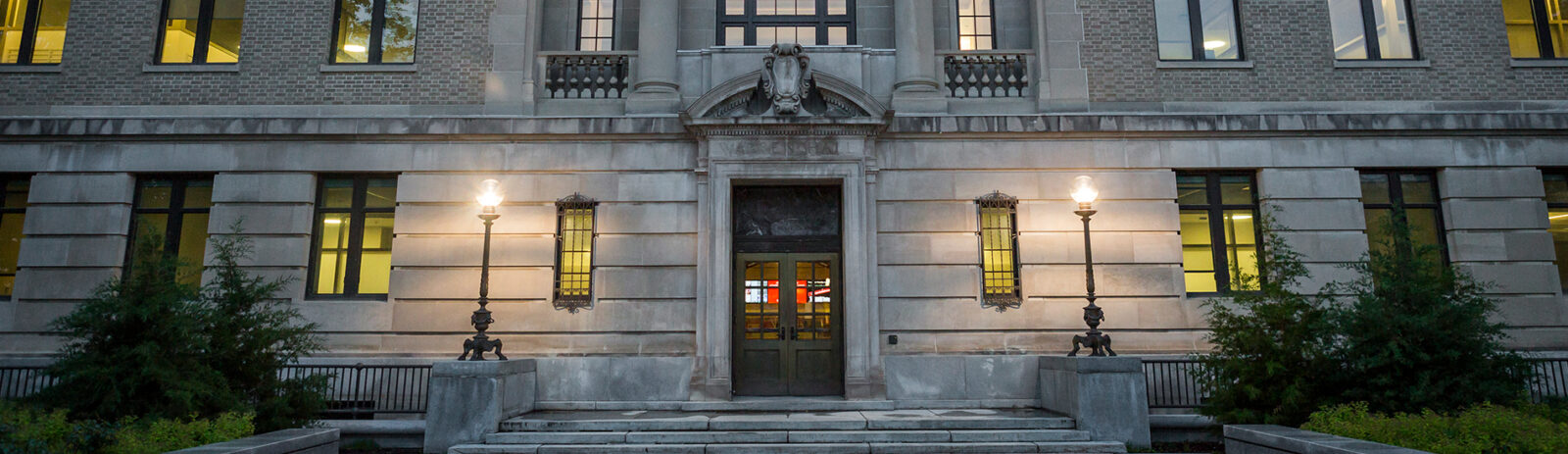 Facade of Warren Hall at night with lights visible through the windows.