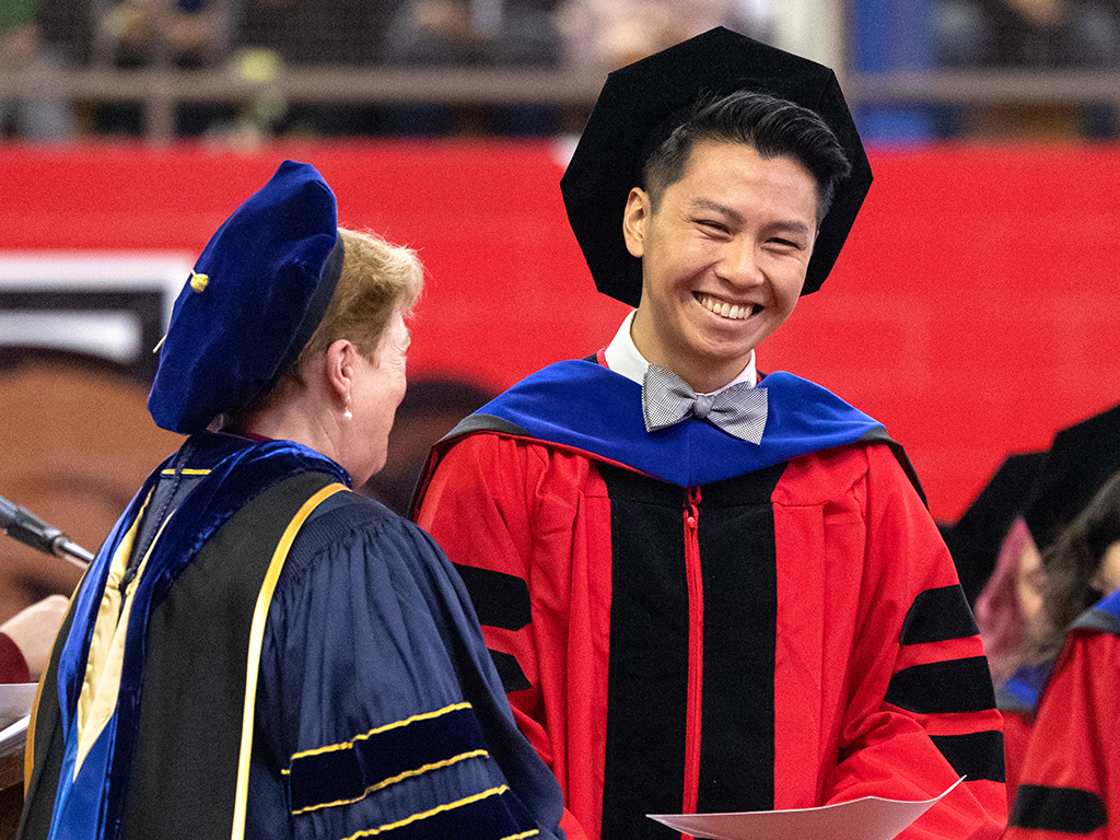 Two people smile in their cap and gowns.