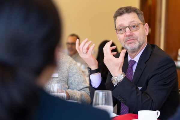 Man wearing a suit sitting at a table talking with his hands.