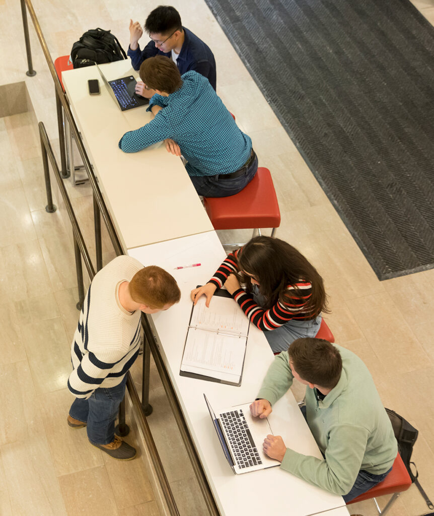 View from above of two groups of people at a long table collaborating around laptops.