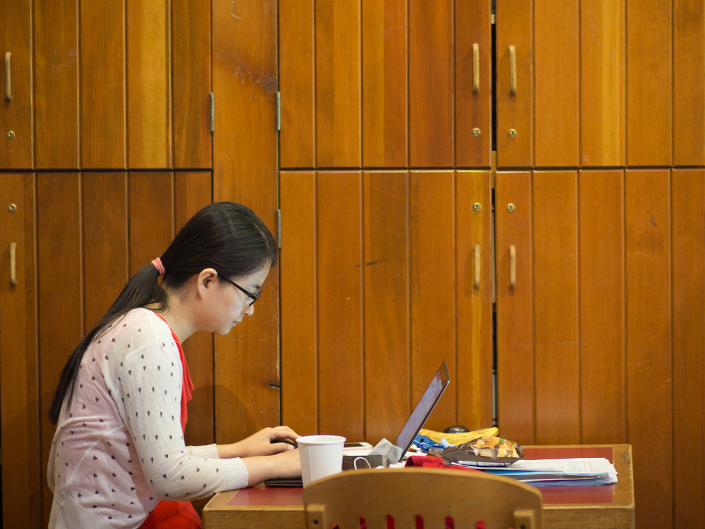 A woman sits at a table alone working on a laptop.
