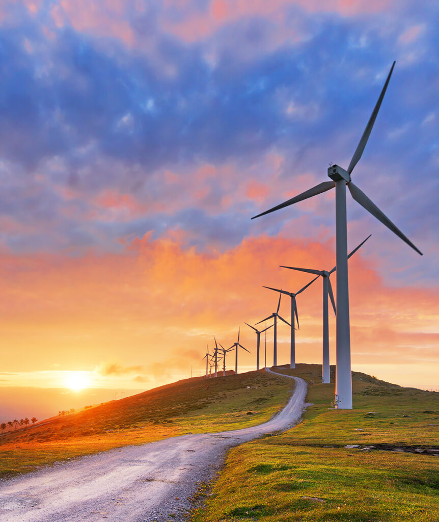 Windmills on a hillside as the sun peaks out from behind the horizon.